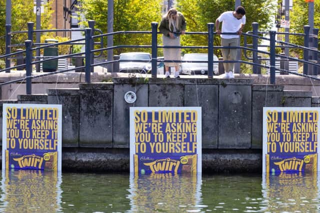 Passersby spot deliberately inconspicuous billboards positioned in the Royal Victoria Dock, Greenwich to mark the launch of the limited-edition Cadbury Twirl Caramel bar. David Parry/PA Wire