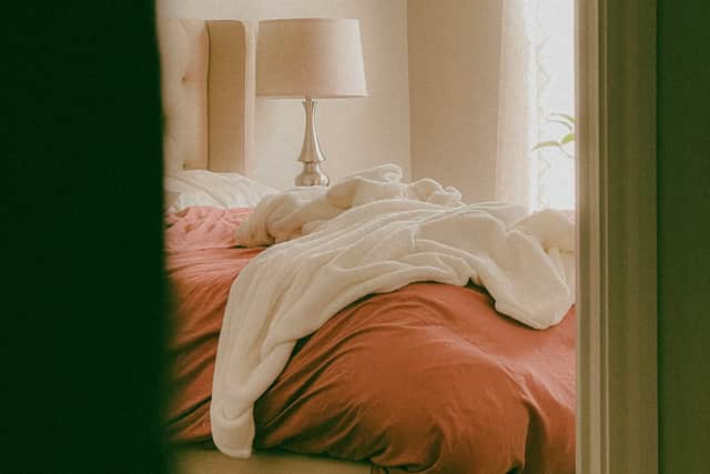 A cozy bedroom featuring an unmade bed with rust-colored bedding and a soft white duvet draped loosely across the mattress. 