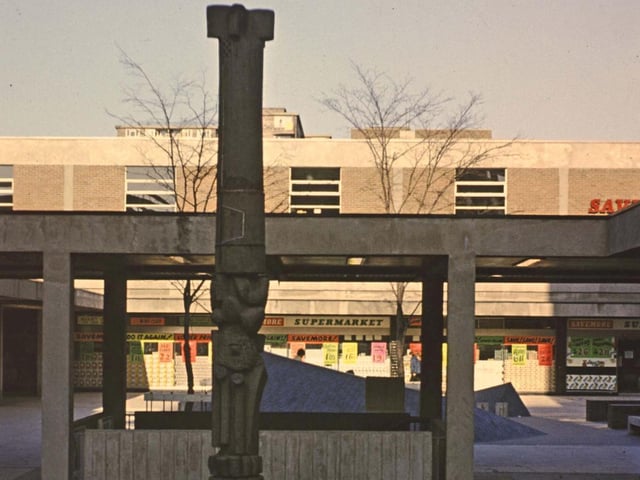 Queen's Parade looking towards Queen's Court in the late 1960s.  A totem pole stands tall in the middle. Savemore supermarket can be seen in the background.