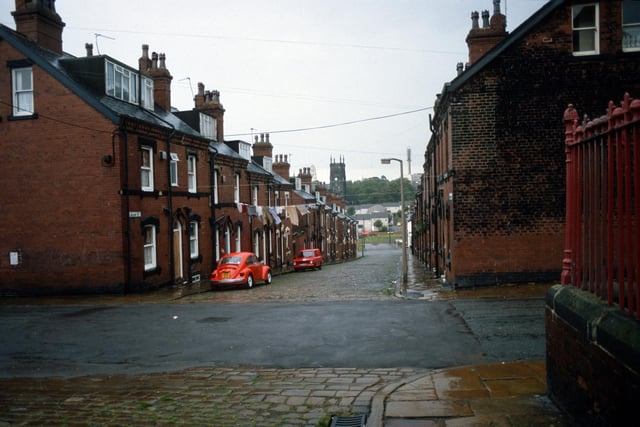 Quarry Street in Woodhouse past the junction with Cross Quarry Street in the foreground pictured in August 1985. A fence on the right encloses the grounds of Quarry Mount Primary School.