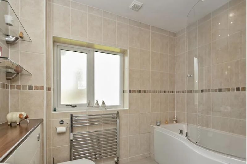 This communal bathroom contains a panelled bath with an over shower and inset wash hand basin with storage underneath. A WC with hidden cistern, tiling to all walls, a frosted window to side, a heated towel rail and tiled flooring.
