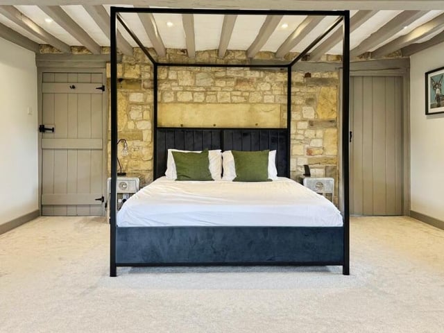 A spacious bedroom with ceiling beams and exposed stonework.