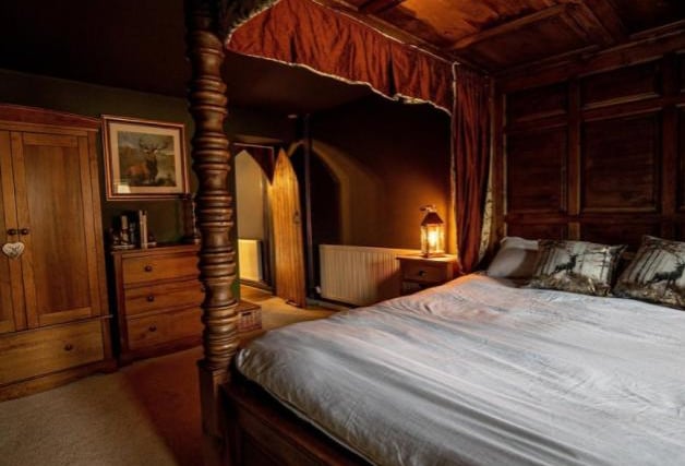 The roundhouse cottage features six handmade wooden four poster single beds each of which have red curtains and bed spreads and golden roman numerals etched on the front of their frames.