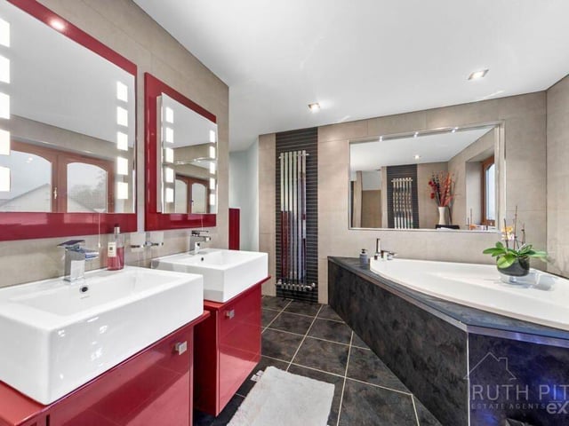 A sleek and luxurious bathroom has a corner bath and twin wash basin vanity units.