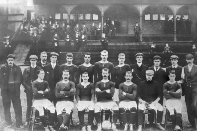 The Hibs team poses for a photo in front of the old east stand in the early 1900s. Possible identities include Pat Callaghan (front row, third from left); James Harrower (front row, second left); Bernard Breslin (front row centre); James Hogg (front row, third right); Robert Glen (back row, fifth left);  Willie Allan (front row, second right); Dan McMichael (back row, third left)