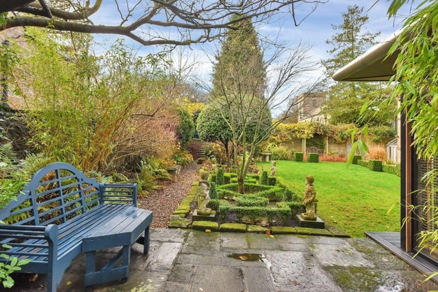 The garden is accessed from a courtyard via stone steps which lead to a lawn with mature beds including shrubs and formal box hedging. A gravel path leads to a flight of stone steps rising to a covered seating area.