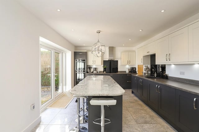 The modern kitchen has a central island, high-spec appliances and is bathed in natural light through the French doors.