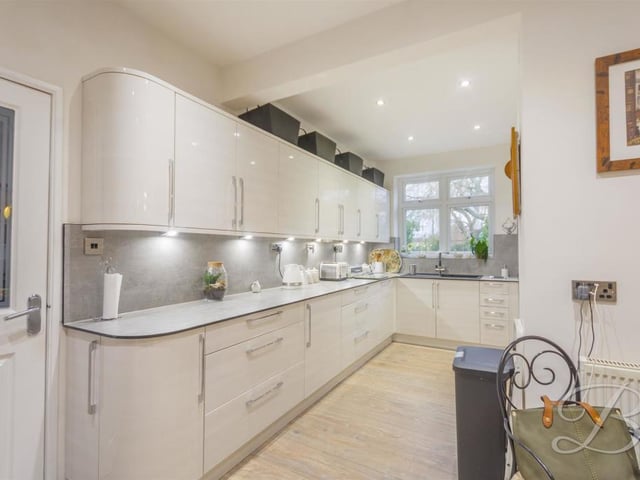 The living room leads to this contemporary kitchen, which is fitted with a range of gloss cabinets offering plenty of storage, a work surface, inset sink and drainer with a chrome mixer tap above, and an extractor fan. The window faces the side of the house.