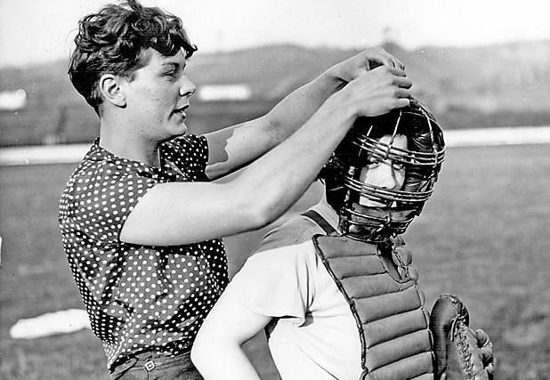 Member of the Sheffield Ladies Baseball Team assisting the 'Catcher' with her face guard, 1937