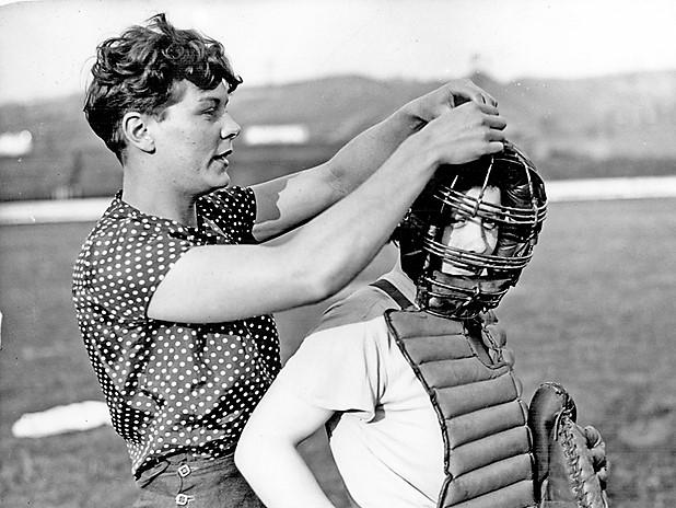 Member of the Sheffield Ladies Baseball Team assisting the 'Catcher' with her face guard, 1937