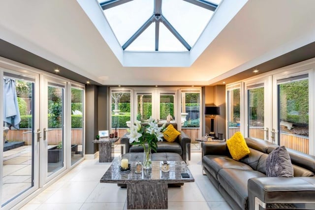 A spacious conservatory or garden room with an atrium ceiling has sets of doors out to the garden.
