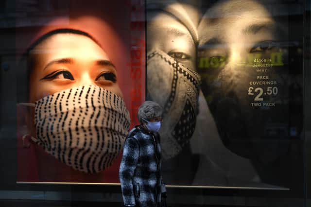 A woman wearing a protective face covering passes a shop window display (Photo by OLI SCARFF/AFP via Getty Images)