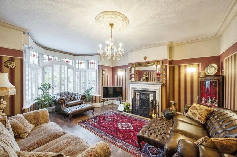The living room with central open fireplace has period decorative features and a large bay window.