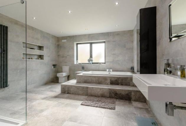 The large family bathroom benefits from a walk-in shower, huge bath, toilet and sink, and modern marble-effect tiling.