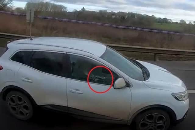 Car driver holding her mobile phone up to talk into as she drives one-handed along the M40