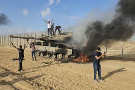 Palestinians celebrate by a destroyed Israeli tank at the Gaza Strip fence east of Khan Younis Saturday, Oct. 7, 2023. The militant Hamas rulers of the Gaza Strip carried out an unprecedented, multi-front attack on Israel at daybreak Saturday, firing thousands of rockets as dozens of Hamas fighters infiltrated the heavily fortified border in several locations by air, land, and sea and catching the country off-guard on a major holiday (AP Photo/Hassan Eslaiah)