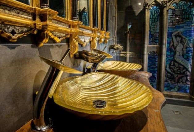 The opulent bathroom features ornate Gothic style mirrors and golden hand basins in the shape of giant shells.