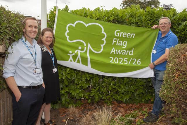 Mathew Gleadall stands next to Suzy Brain England OBE with Martin Smith, Trust Gardener, holding the Green Flag Award flag for 2025/26.