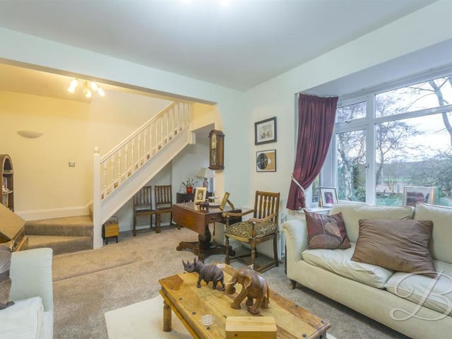 The living room from a second angle, showing the beautiful bay front window, which floods in plenty of natural light, creating the perfect environment for entertaining guests. The floor is carpeted and the staircase lead to the first floor.