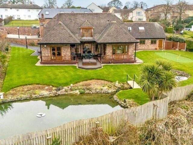 An overview of the rear of the home, with a feature pond and putting green in a landscaped garden.