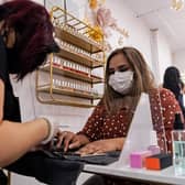 A nail technician wearing a face mask or covering due to the COVID-19 pandemic, sits behind a perspex safety screen as she paints the nails of a customer (Photo by NIKLAS HALLE'N/AFP via Getty Images)