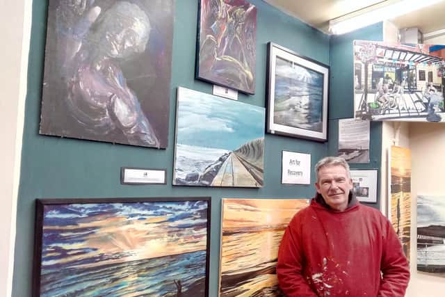 Andy Hollinghurst next to the wall of of paintings showing how his mind improved after a nervious breakdown