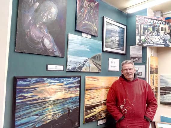 Andy Hollinghurst next to the wall of of paintings showing how his mind improved after a nervious breakdown