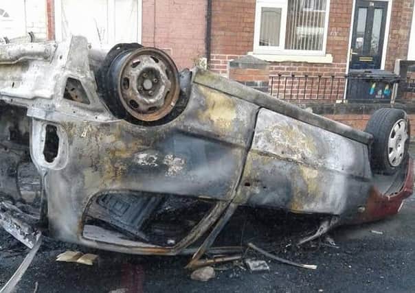 A burnt-out car is upside down on the footpath