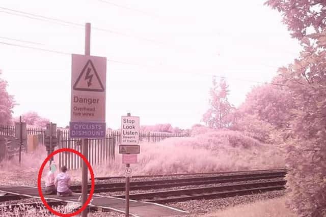 Two youngsters are pictured sitting in the middle of the East Coast Main Line.